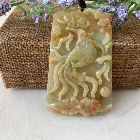 Close-up of carved red and yellow jadeite phoenix pendant with polished translucent finish on woven display background