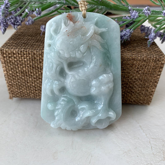Close-up of pale green jadeite jade dragon pendant, hand-carved glossy finish, front view on cord, decorative backdrop