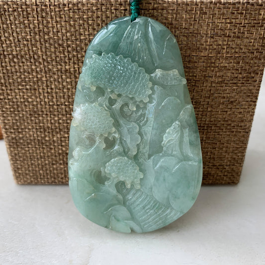 Front view of translucent green jadeite pendant with hand-carved mountain forest river scene and polished finish
