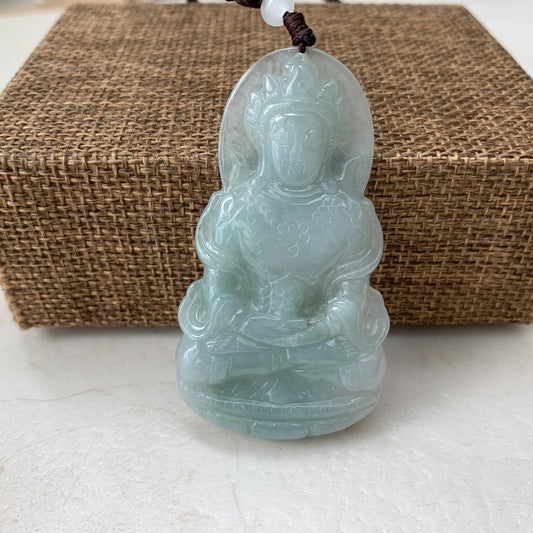 Front view of pale green jade Guan Yin carved pendant necklace with glossy finish and braided cord on woven mat