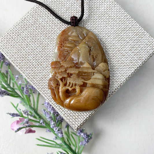 Close-up of hand-carved yellow and red jadeite pendant necklace with glossy landscape mountain forest river relief on cord