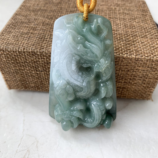 Close-up of hand-carved jadeite jade dragon pendant necklace with glossy green-white finish and gold cord