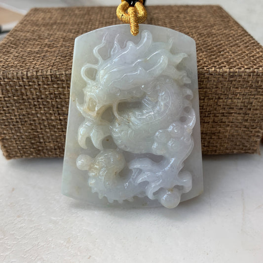 Close-up of translucent white jadeite dragon pendant with carved relief and gold cord on woven background