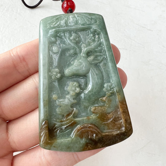 Close-up of hand-carved green jadeite pendant with deer in forest relief, glossy polished finish, on cord necklace