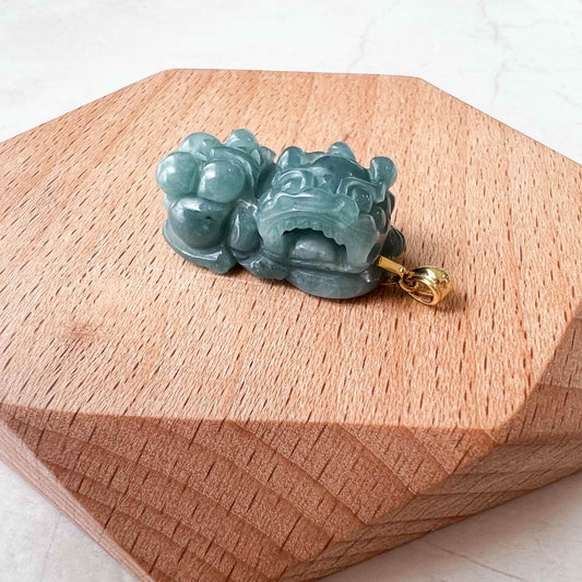 Blue green jadeite jade dragon pixiu pendant side view with glossy carved finish and 18k gold bail on wooden board